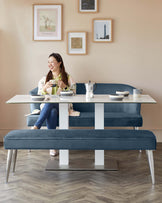 Contemporary dining furniture set including a rectangular white dining table with sleek silver legs and a long blue upholstered bench with a button-tufted seat and metallic silver legs.