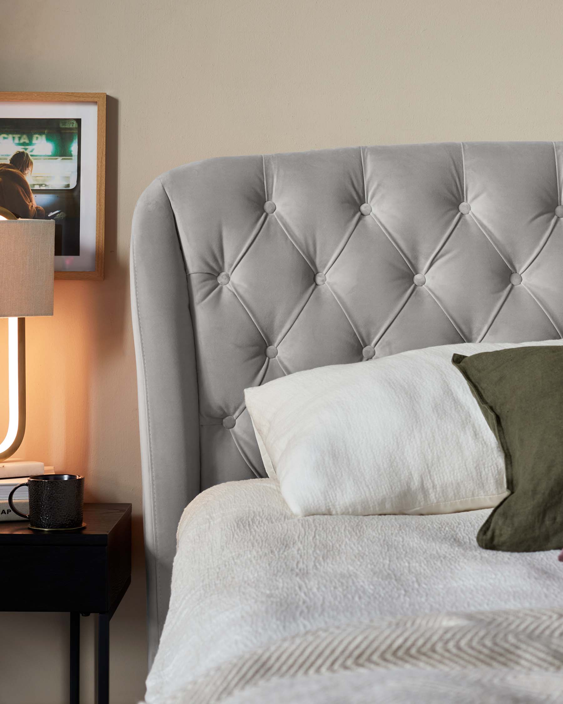 Elegant grey tufted headboard, black bedside table with a modern lamp, and decorative framed artwork.