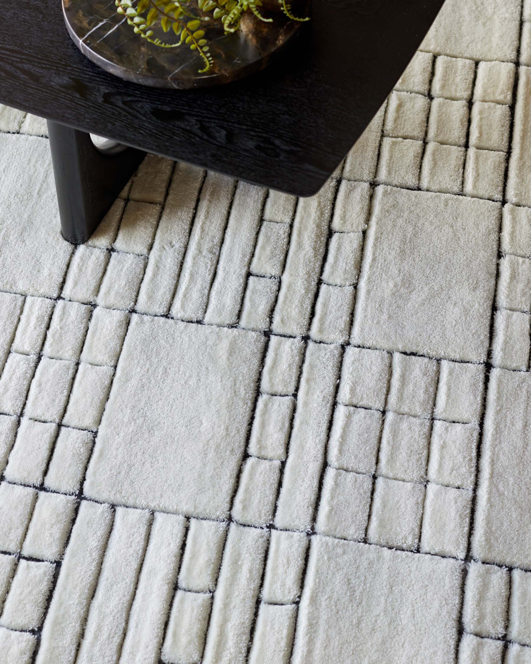 Close-up of a textured contemporary area rug and a portion of a modern dark wood coffee table with a round decorative bowl on top.