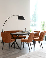 Modern dining room furniture set featuring a dark wooden table with a unique X-shaped black metal base. Surrounding the table are four elegant dining chairs with a burnt orange upholstered fabric, quilted backrests, and tapered black metal legs. An arched floor lamp with a large black shade extends over the table, adding a contemporary touch to the space.