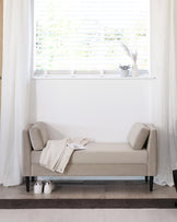 Elegant upholstered bench with bolstered ends, a cozy throw, and nearby shoes, enhancing a bright, minimalist space.