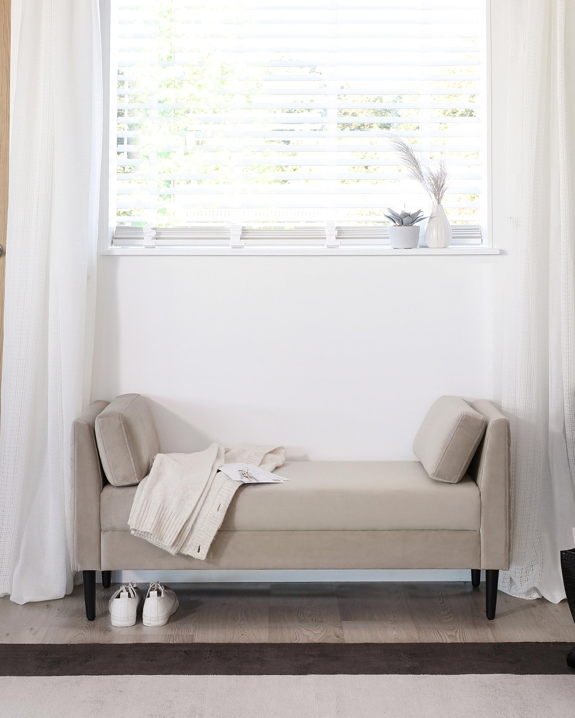 Elegant upholstered bench with bolstered ends, a cozy throw, and nearby shoes, enhancing a bright, minimalist space.