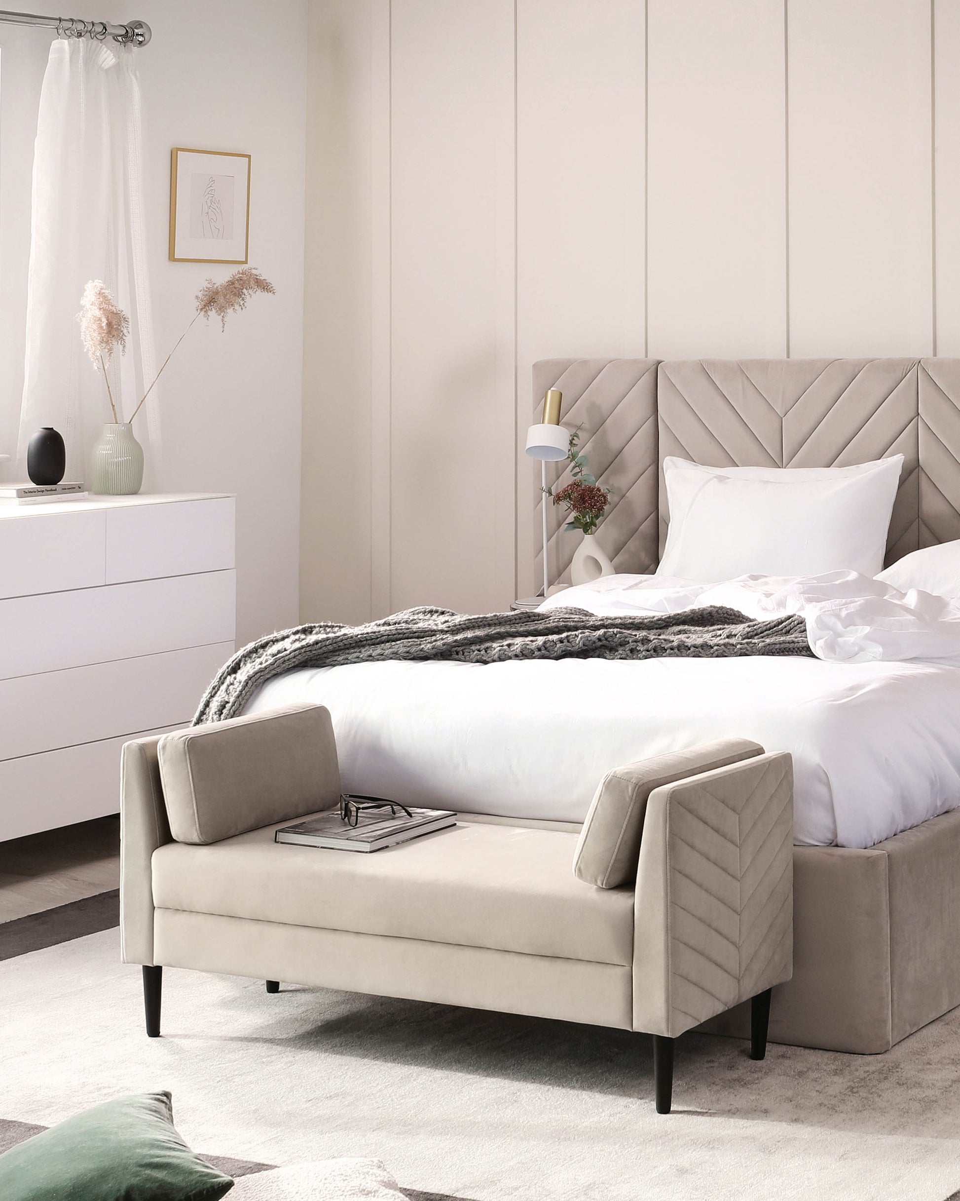 Stylish beige upholstered bench with two back cushions, positioned in a modern bedroom with a plush bed and minimalist decor.