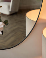 Contemporary round pedestal side table in a soft beige finish, with a reflective round tabletop mirror, featuring a minimalist aesthetic.