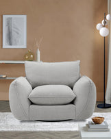 A plush, light gray armchair with a rounded design and oversized cushions, set on a textured rug next to a modern floor lamp.