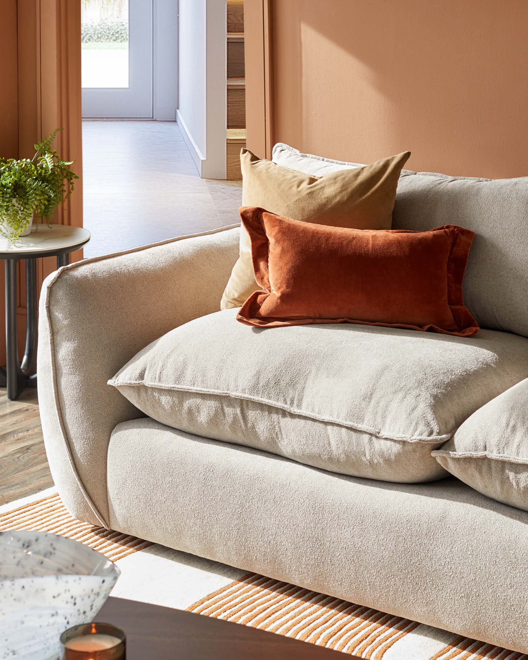 Cozy beige sofa with plush cushions and decorative pillows in earthy tones, paired with a sleek side table and patterned rug.