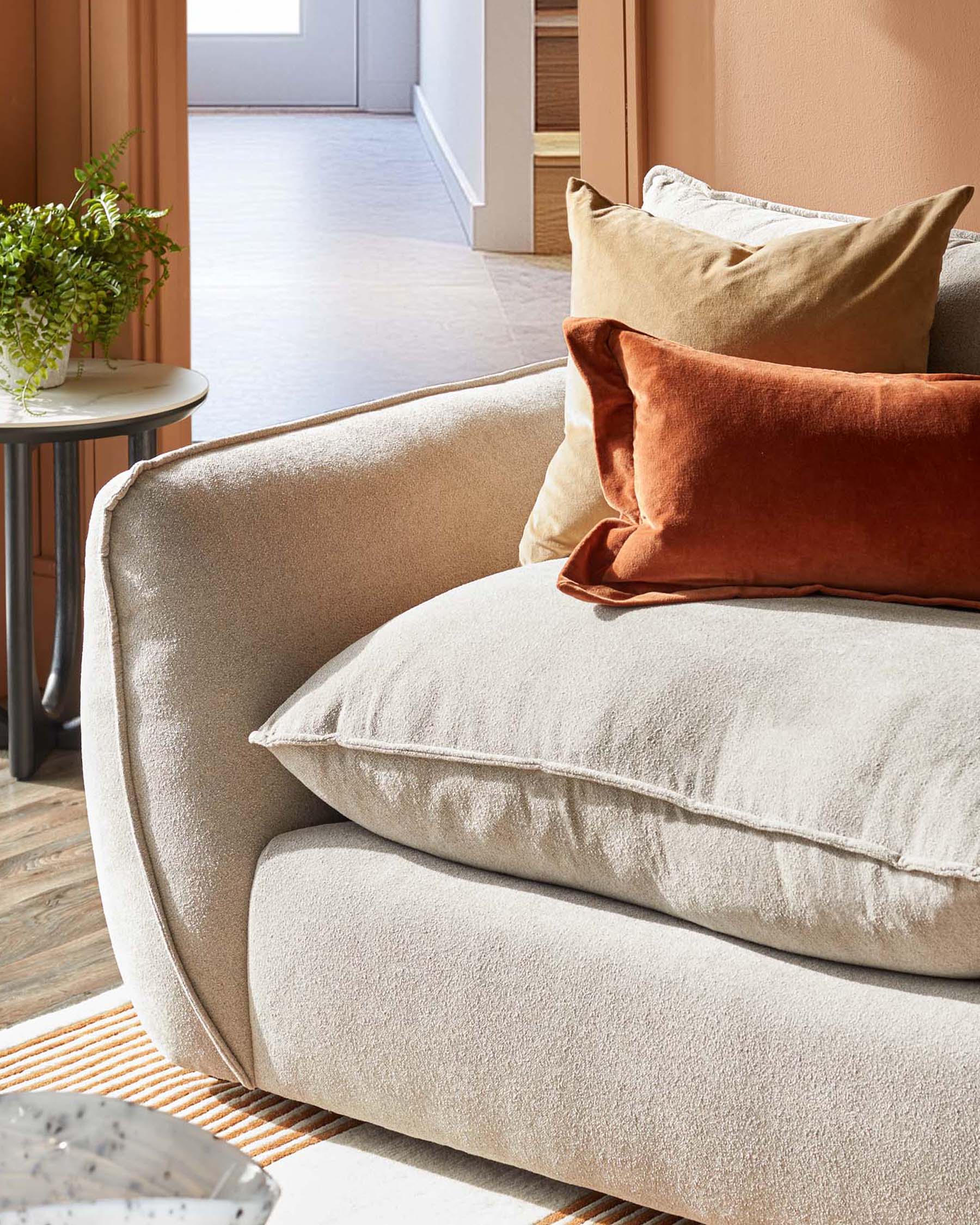 A plush beige sofa with luxurious throw pillows in earthy tones, paired with a stylish round side table and green plant.