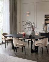 Elegant dining room setting featuring a dark, rectangular wooden table with unique, curved black legs, surrounded by four plush beige upholstered chairs with smooth curves and black wooden legs. A textured grey vase with dried branches is placed on the table, complemented by a red candle holder. The room has a contemporary aesthetic with neutral tones and natural light filtering in through sheer curtains, highlighting the clean lines and sophisticated design of the furniture.