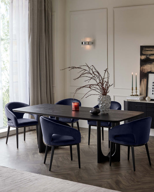 A sleek dark wooden dining table surrounded by four navy upholstered chairs, accented with decorative vases and candles.