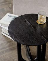 A sleek, modern round side table with a dark wood textured surface on a sturdy black base.