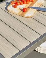 A modern, slatted table surface with a gray finish, complemented by a wooden cutting board and fresh cherry tomatoes.