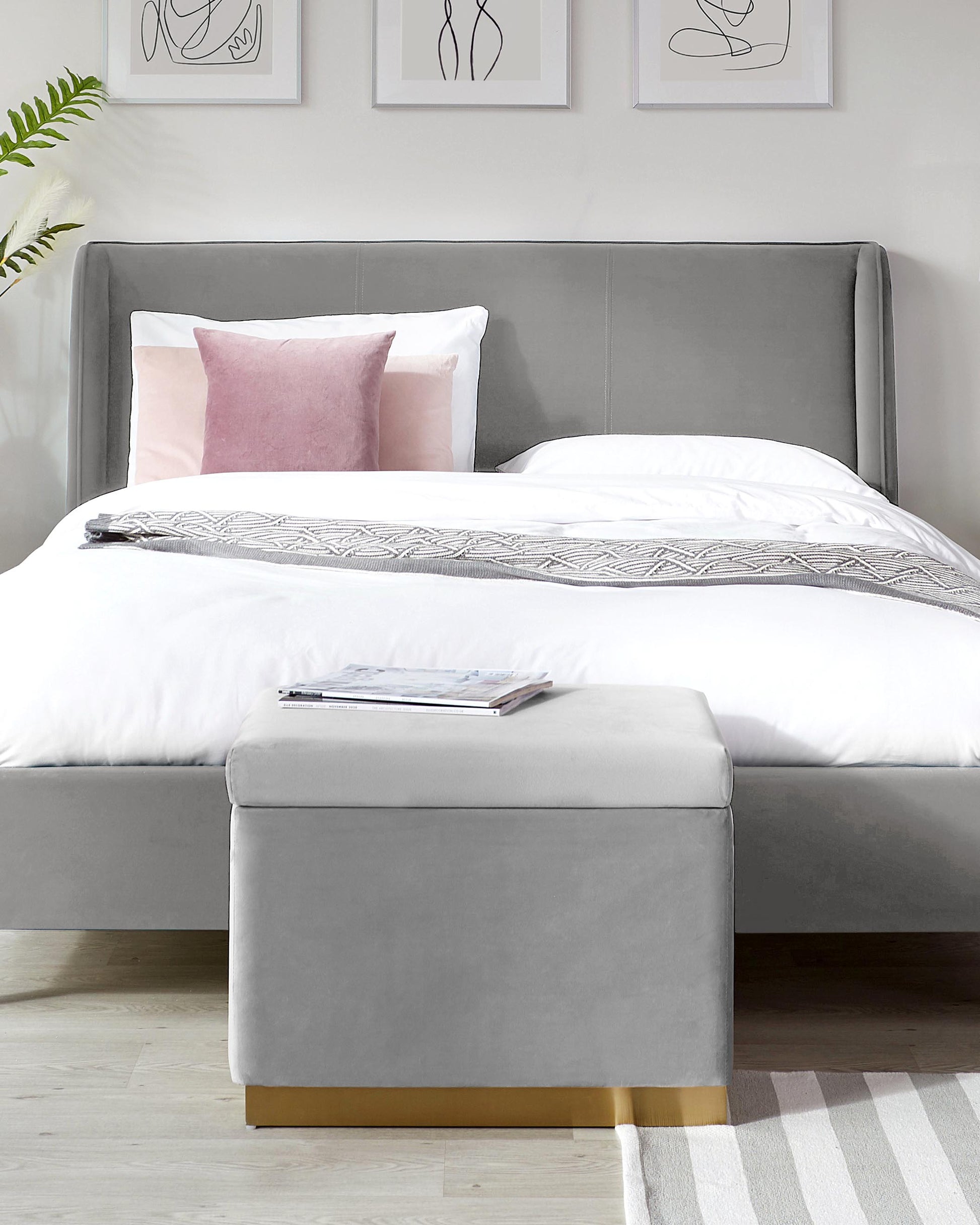 Stylish gray upholstered bed with white bedding, accent pillows, and a coordinating storage ottoman with gold accents.