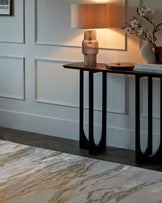 Elegant slim console table with a dark wood top and curved black metal legs, accompanied by decorative accessories including a sculptural table lamp and books.