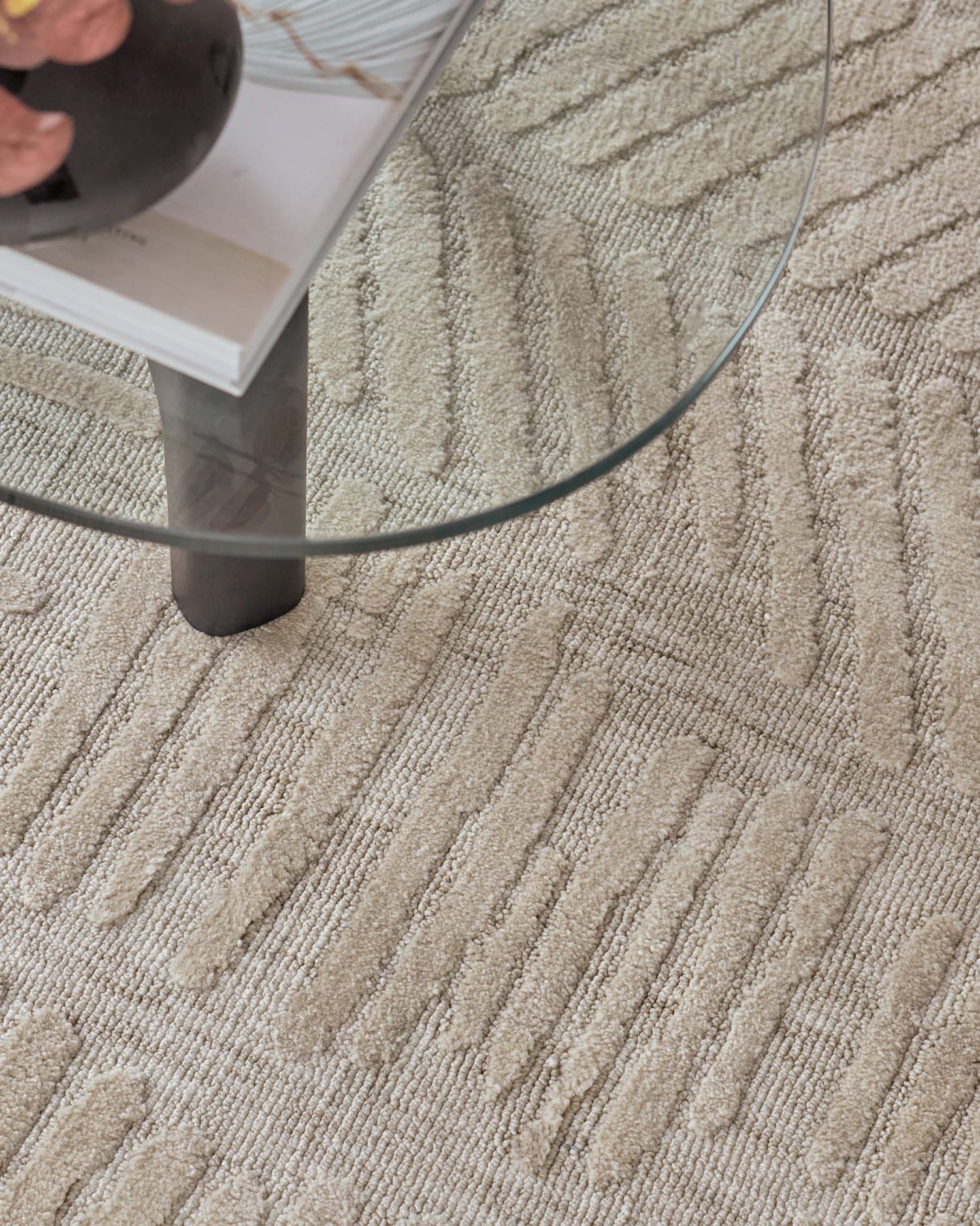 Modern oval glass coffee table with a sleek metal leg and a lower white shelf, standing on a textured beige carpet.