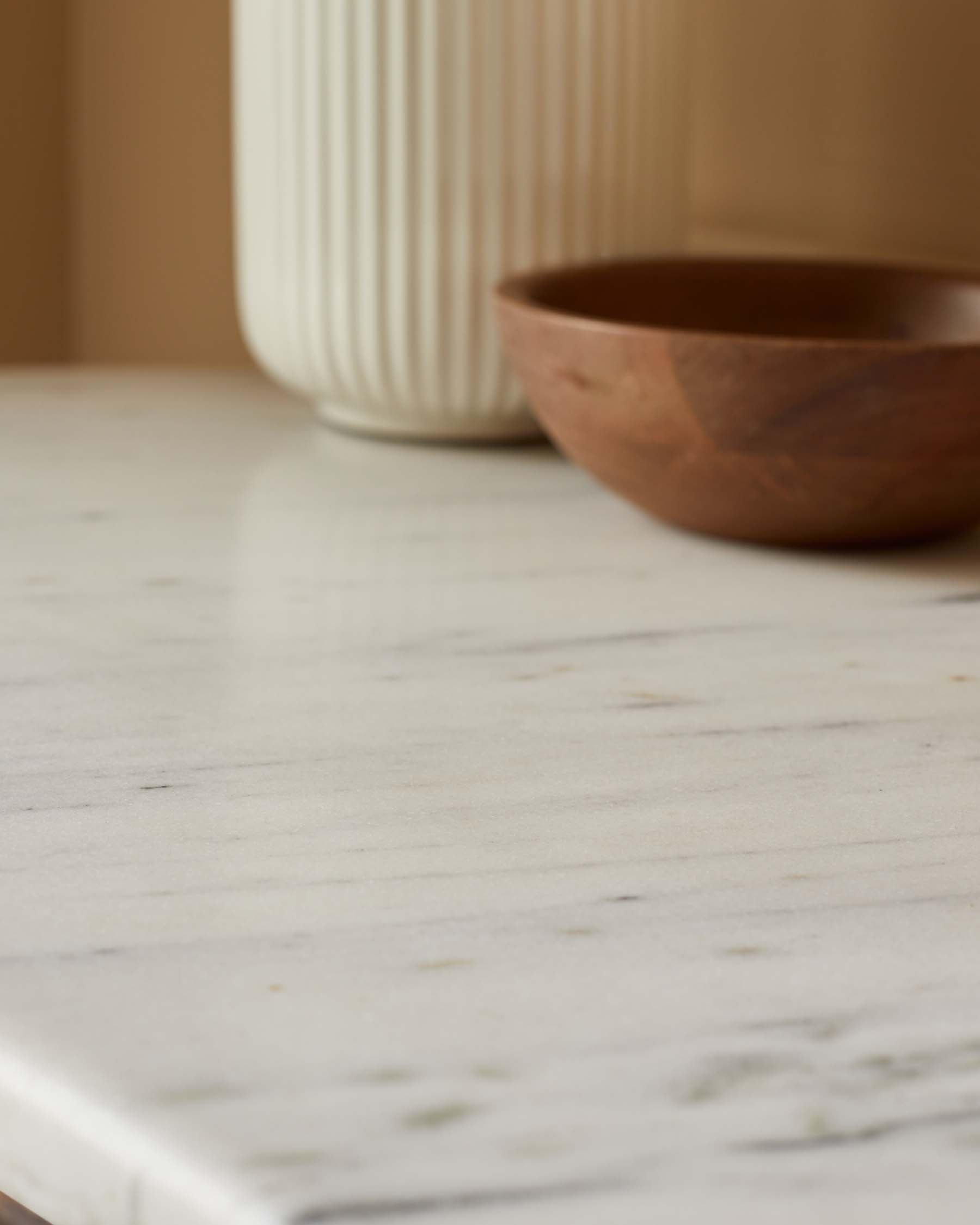 A smooth marble surface with a white ribbed vase and a textured wooden bowl for a modern, elegant display.