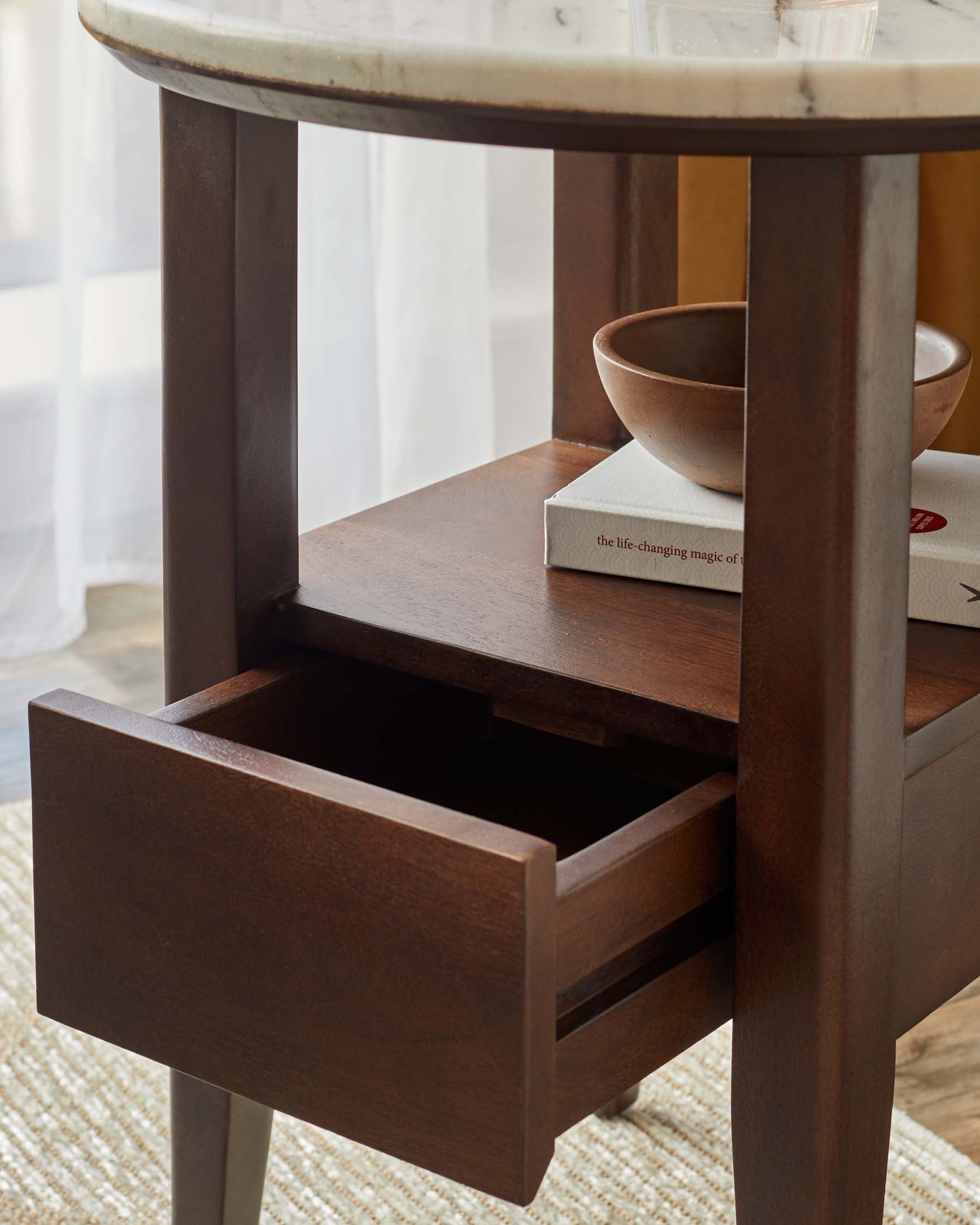 Elegant side table with a marble top, wooden base, open shelf, a drawer, a decorative bowl, and books on display.