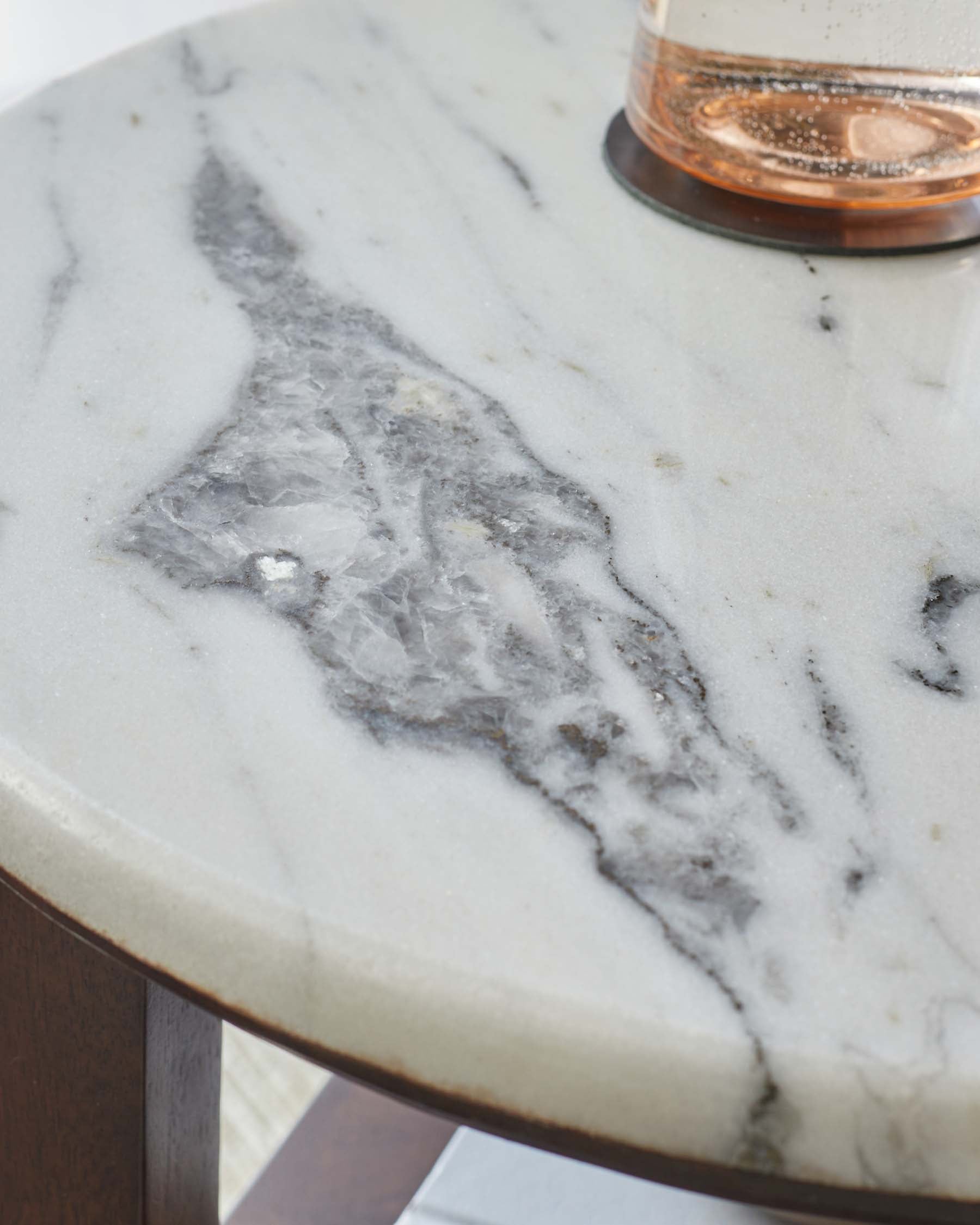 Close-up of a polished marble tabletop featuring a unique gray and white pattern, complemented by a glass.