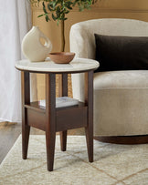 A sleek side table with a marble top, wooden legs, and a lower shelf, paired with a cozy, curvy armchair with a dark cushion.