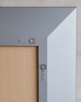 The image shows a close-up detail of a piece of furniture focusing on its construction. Visible is a grey painted corner of a wooden panel with a metal bracket for structural support. The bracket has a small cut-out handle, suggesting the piece is part of a larger item, possibly a cabinet, door, or drawer, demonstrating the furniture's durability and thoughtful design.