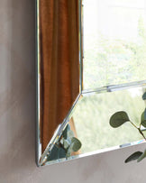 Modern reflective mirror with a sleek metallic frame, positioned near a window to enhance natural light in the room.