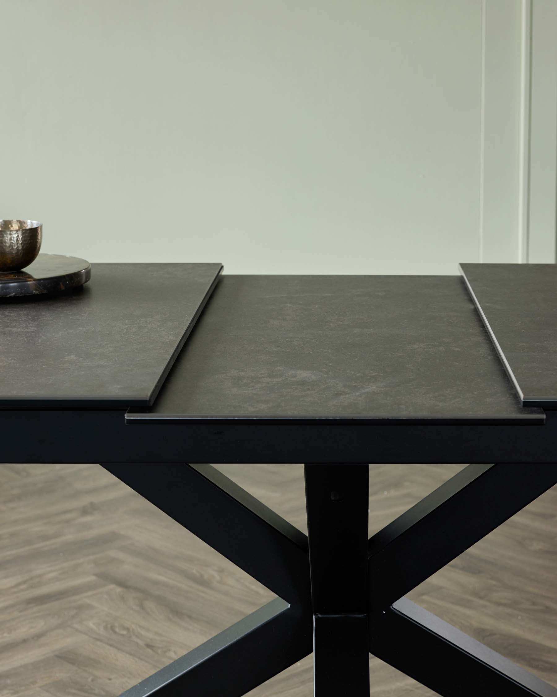 A sleek, modern black table with a cross-base, featuring a textured top and decorative bowl on a round plate.