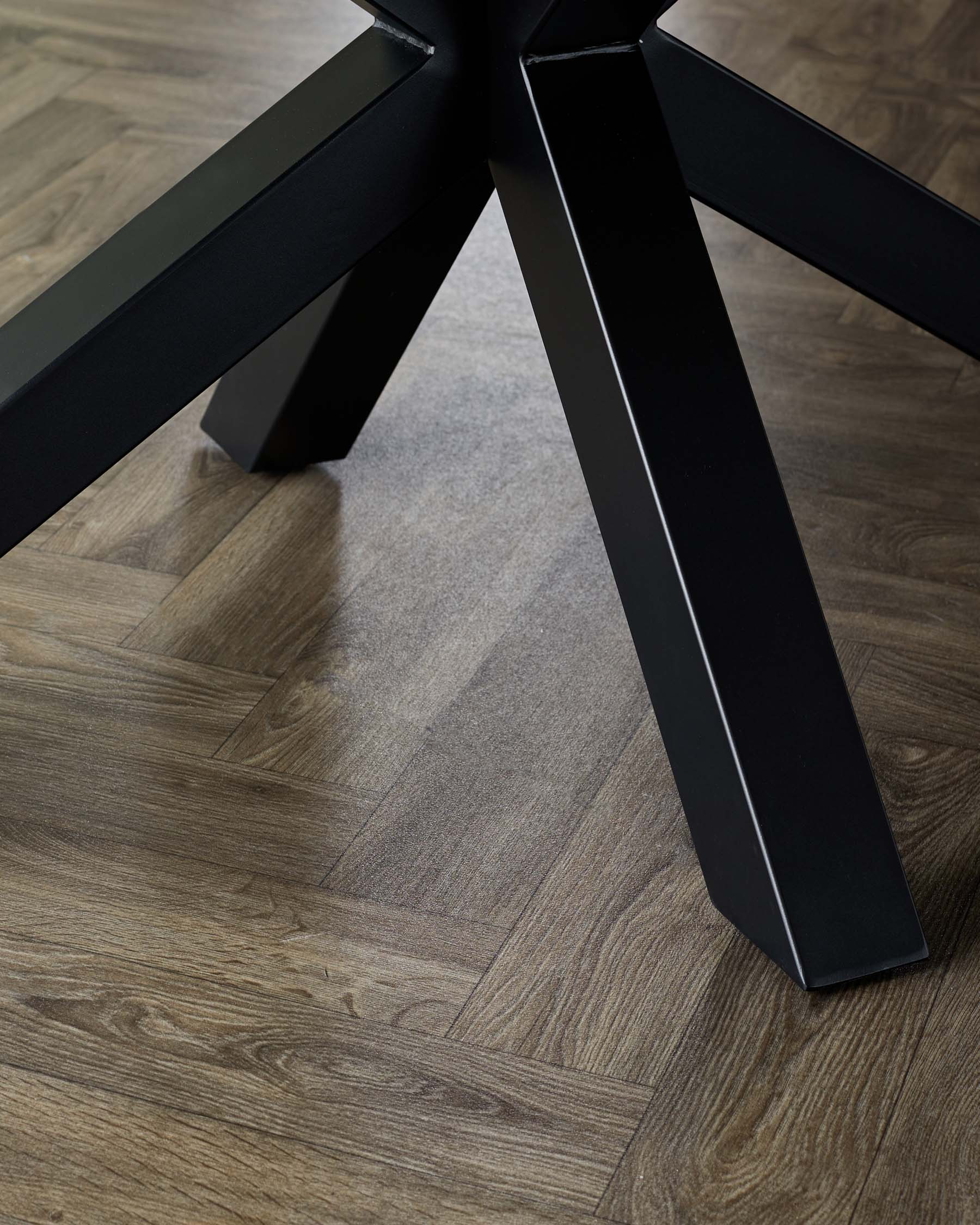 Close-up view of a modern matte black table leg with a sleek, angular design on wooden flooring.