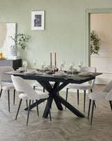 A modern dining set featuring a rectangular black table with a unique, intersecting X-shaped base design, paired with six light grey upholstered chairs with slim black metal legs. The table is set for a formal meal with plates, glasses, and candlesticks.