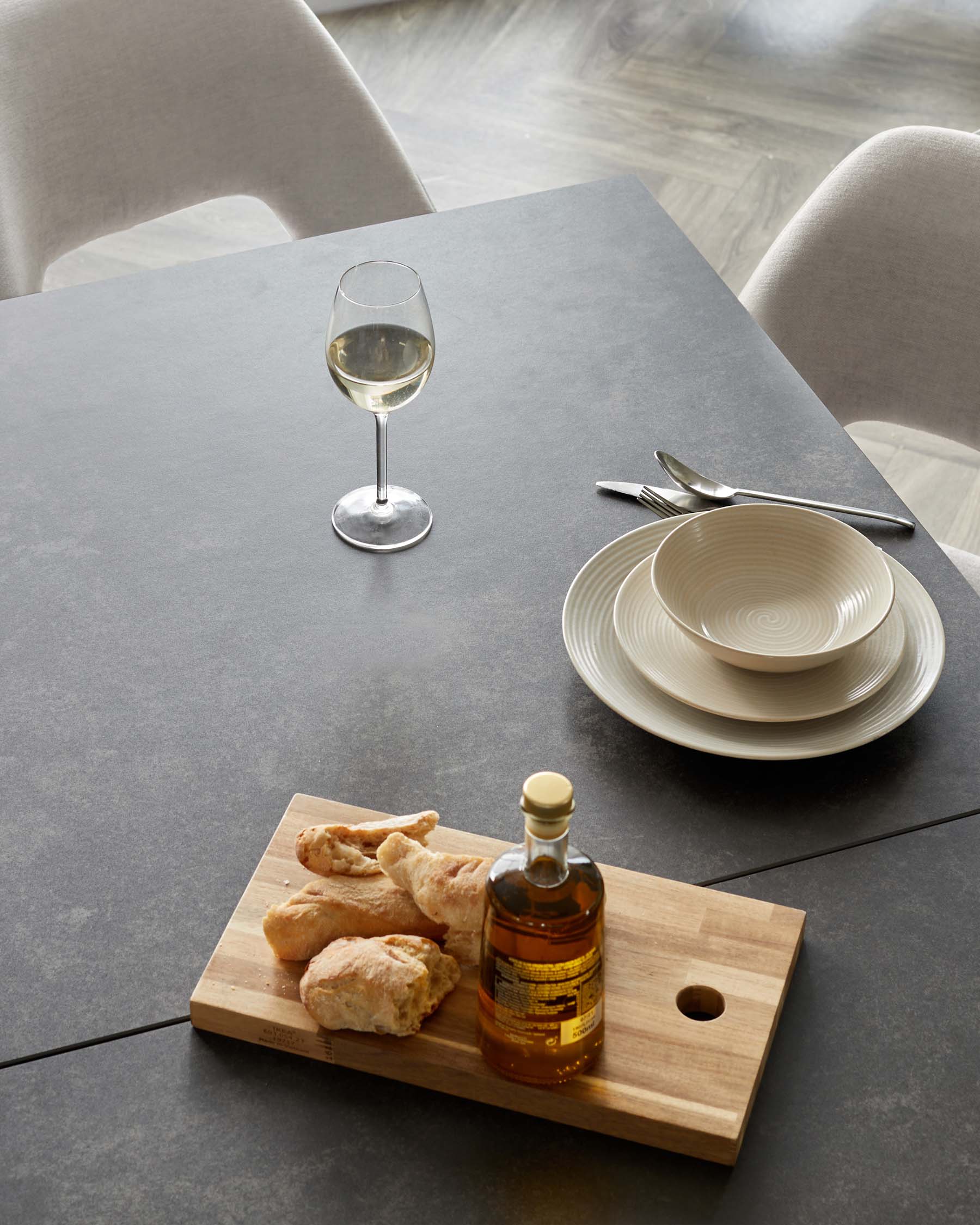 Modern minimalist dining table with a smooth, dark grey surface complemented by light grey, fabric upholstered chairs with a contemporary design.