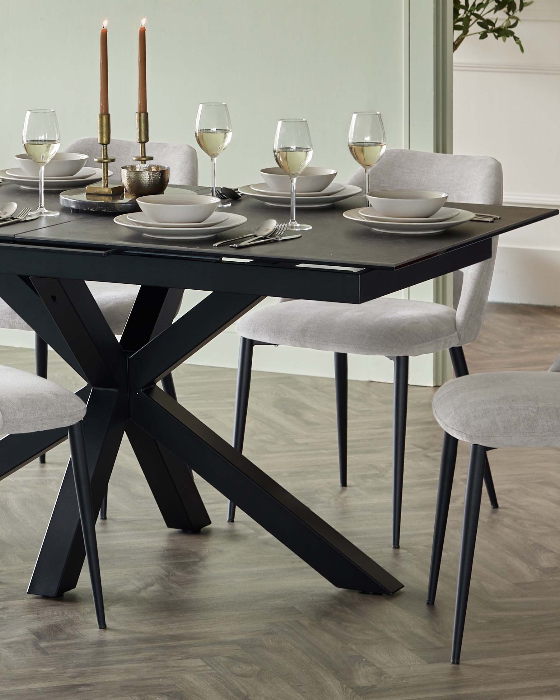 A modern dining set featuring a sleek black rectangular table with a unique star-shaped base and a set of four matching grey upholstered chairs with slim black metal legs. The table is elegantly set with dinnerware, glassware, and a pair of candles; creating an inviting atmosphere.