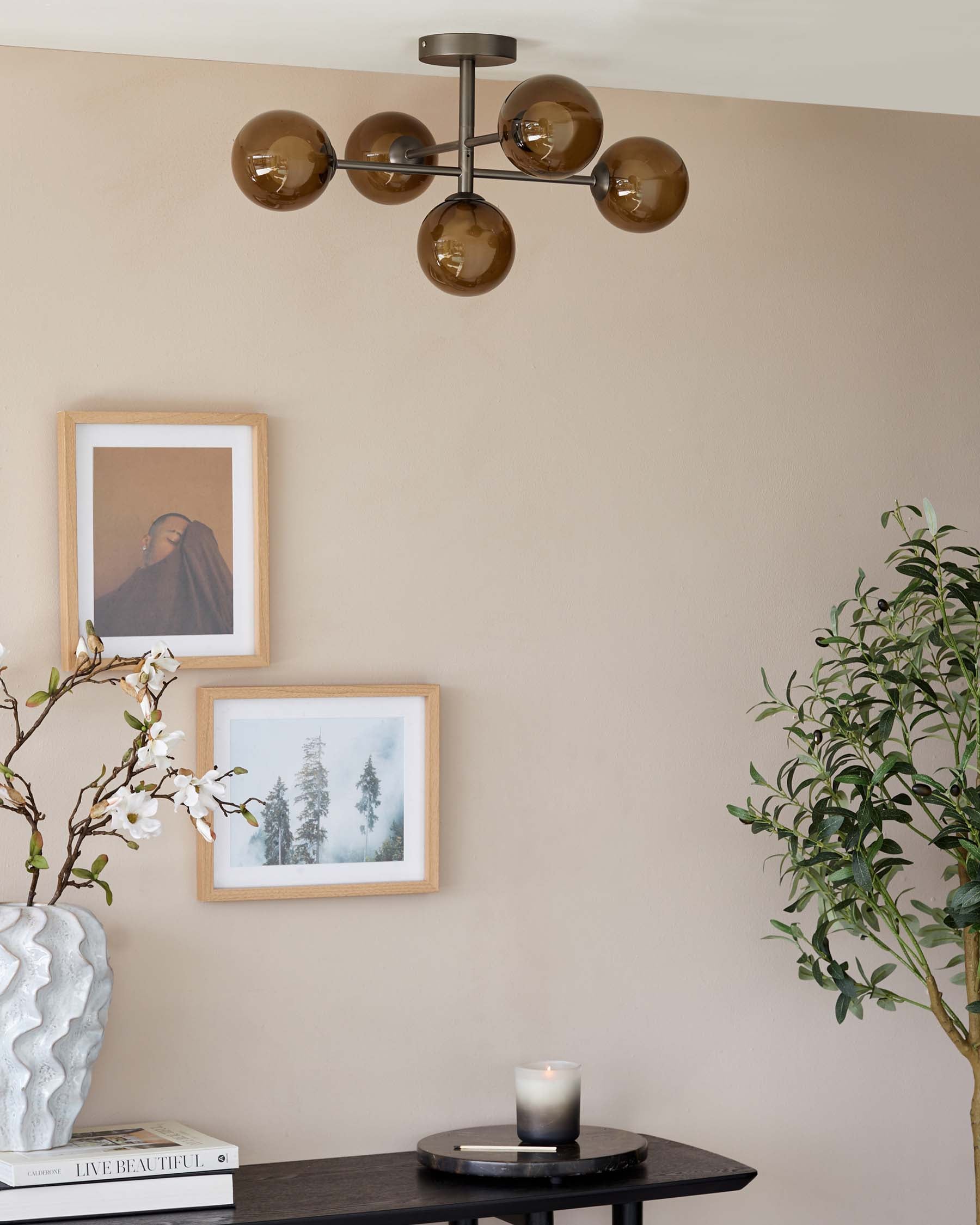 Modern black round side table displaying a decorative vase, books, and a lit candle, complementing an interior space with earth-toned walls and framed artwork.