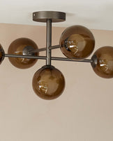 Modern chandelier with a metallic structure and five spherical, smoked glass shades attached to arm-like extensions, mounted on a ceiling.