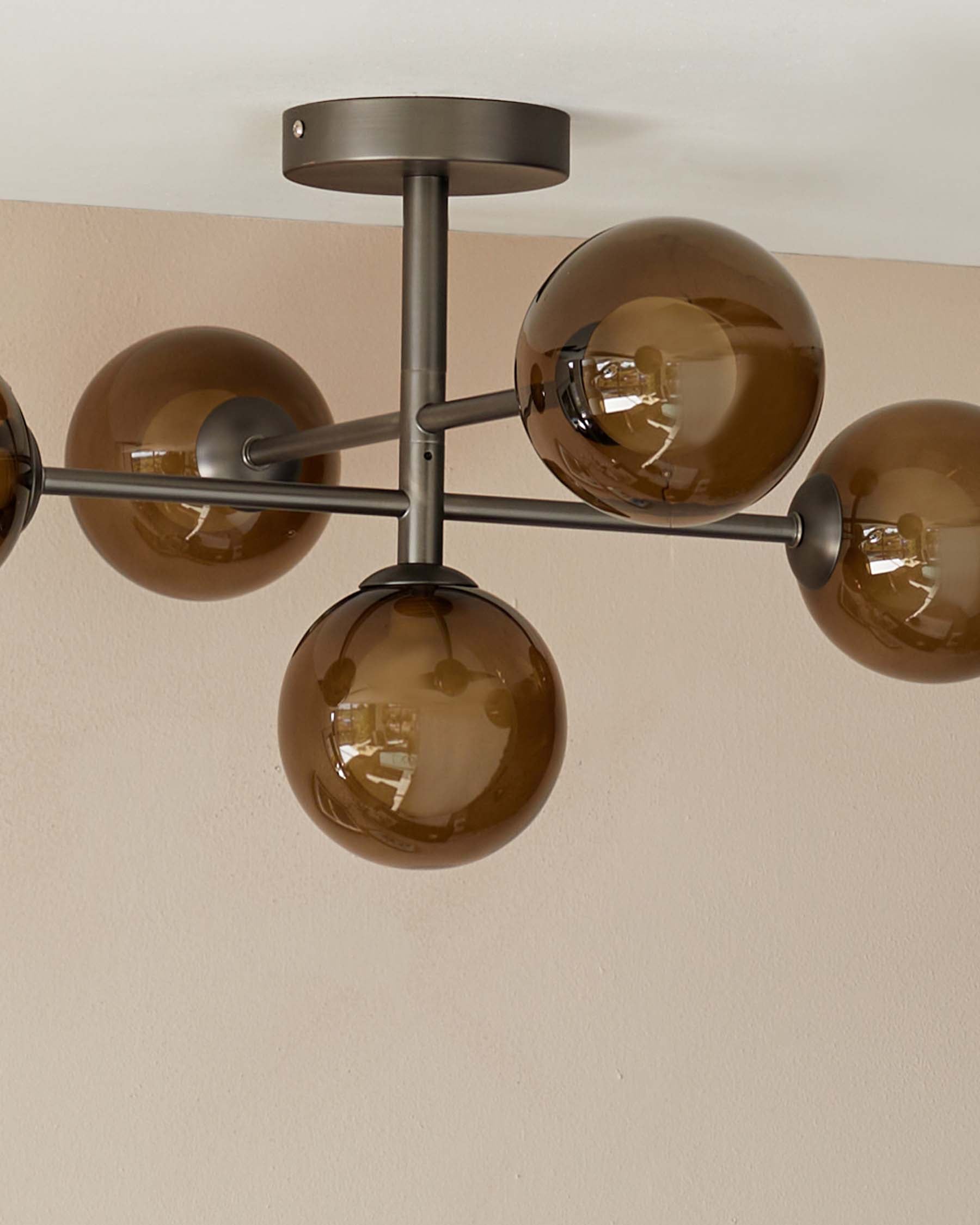 Modern chandelier with a metallic structure and five spherical, smoked glass shades attached to arm-like extensions, mounted on a ceiling.