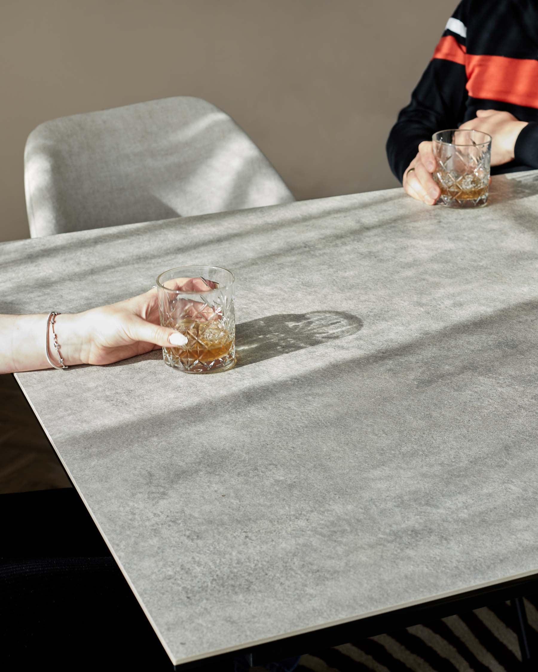 A modern rectangular dining table with a sleek, stone-like finish and thin black legs, accompanied by a high-back dining chair upholstered in light grey fabric.