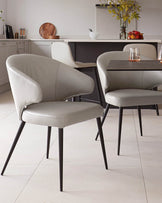 Sleek, modern dining chairs with gray leather upholstery and slender black legs, paired with a simple black table.