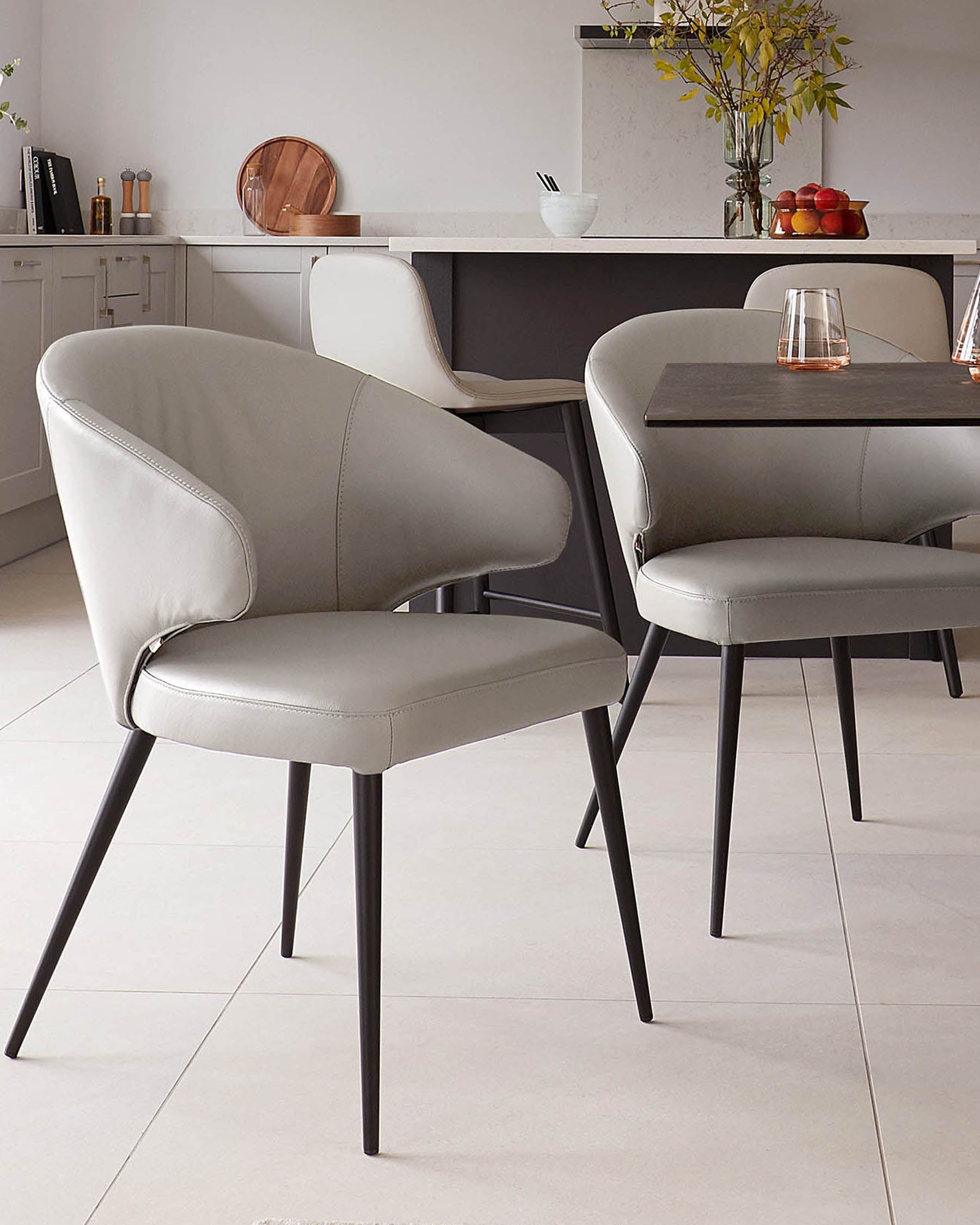 Sleek, modern dining chairs with gray leather upholstery and slender black legs, paired with a simple black table.