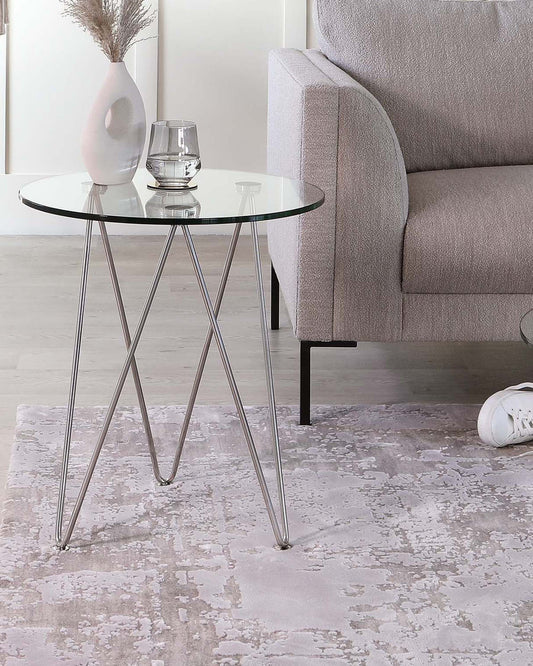 A stylish gray couch beside a glass-top side table with metal legs, complemented by a decorative vase and glass.