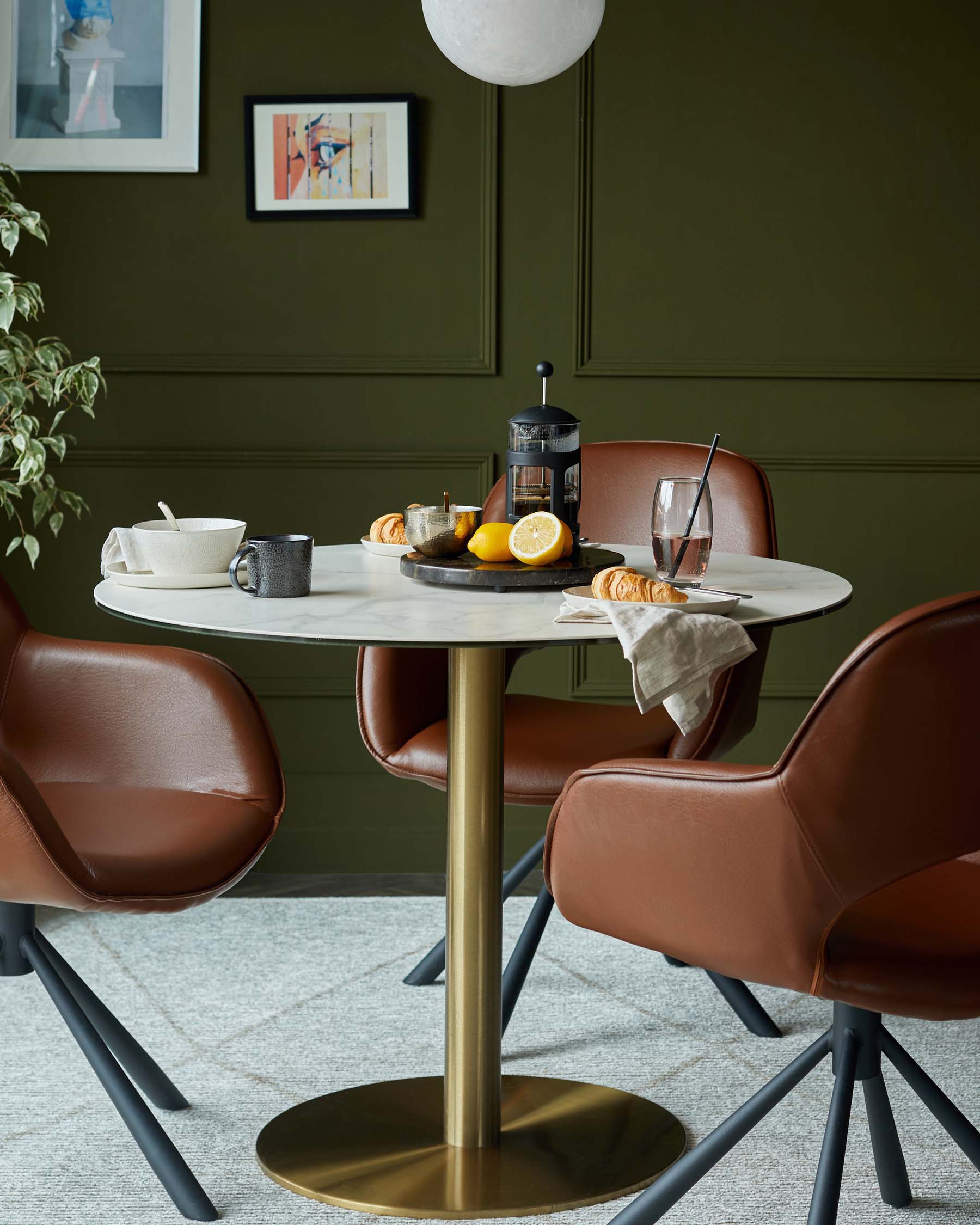 Round marble dining table with a gold base, paired with brown leather chairs, set with drinks and pastries.