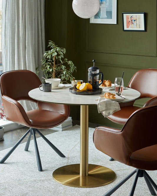 Stylish round marble table with a gold base, surrounded by modern brown leather chairs, creating a cozy dining space.