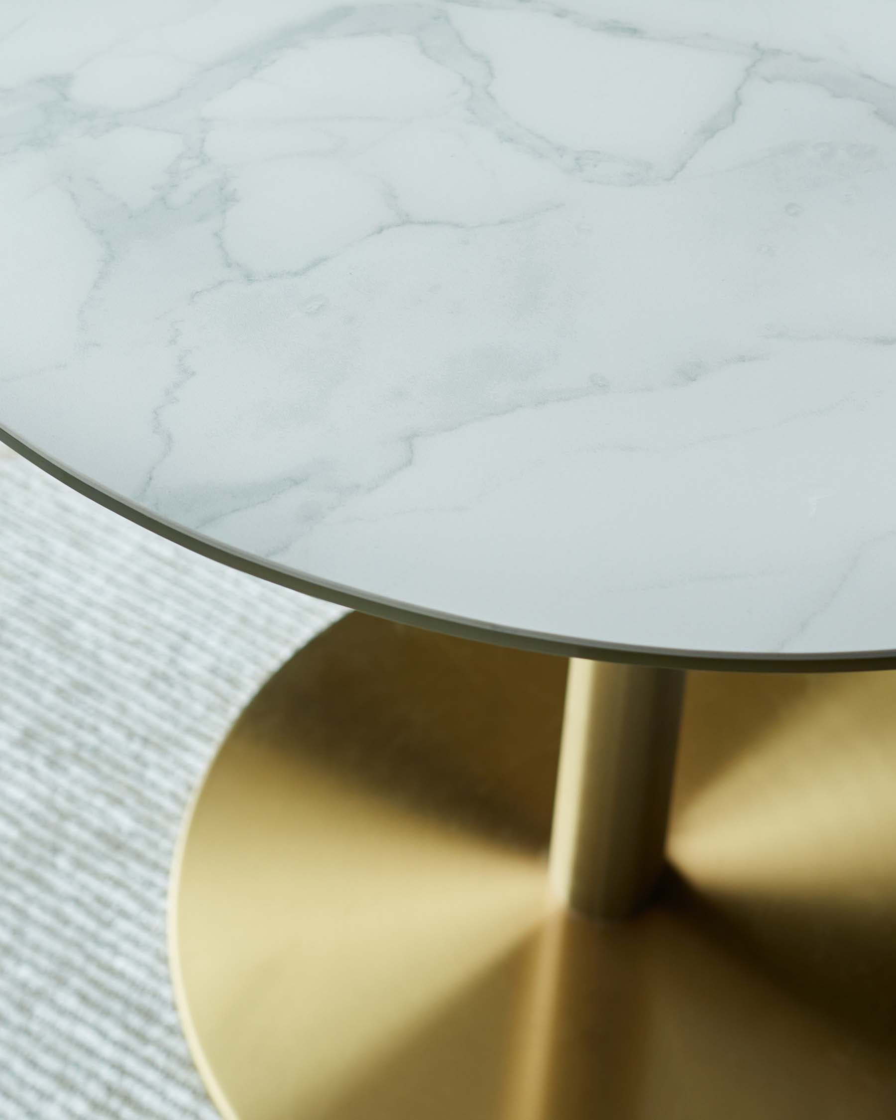 A modern round coffee table featuring a sleek white marble top supported by a polished gold metal base.