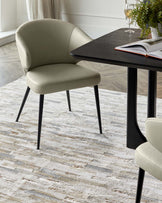 Modern dining room with a dark wooden table featuring sleek black legs, complemented by two olive green upholstered chairs with a curved backrest and elegant black metal legs. The setting is on a textured off-white area rug.