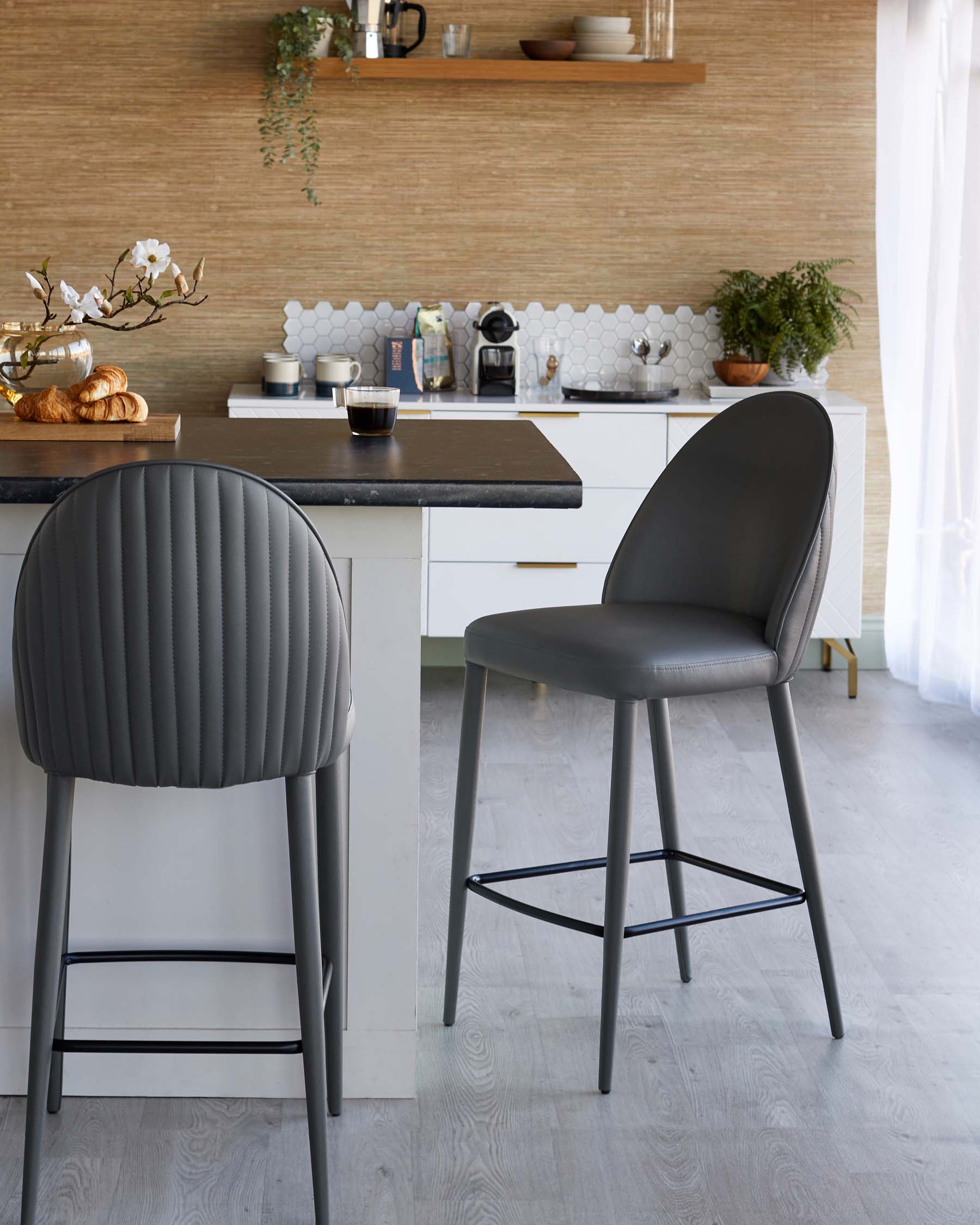 Two modern gray barstools with ribbed backs, paired with a sleek kitchen island, complemented by minimalist decor and natural elements.