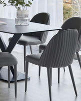 Stylish gray dining chairs with ribbed design around a sleek, modern black table, topped with decorative glass vases and foliage.