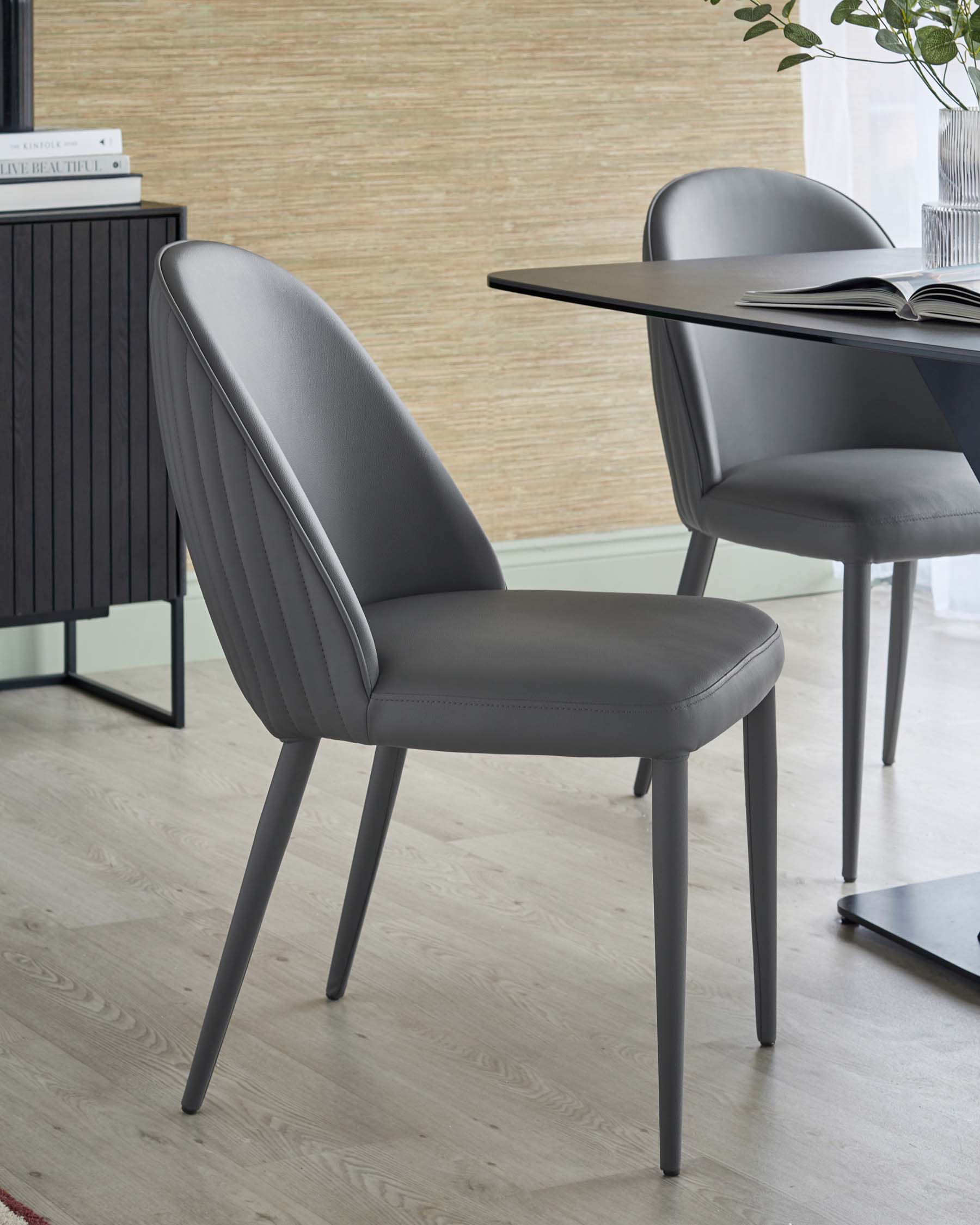 Sleek grey dining chair with a curved back, ribbed design, and thin, tapered legs, paired with a minimalist dining table.