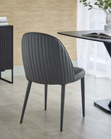 A sleek, modern gray upholstered chair with vertical ribbing and slender legs, positioned near a minimalistic black table.