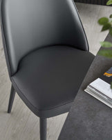 Contemporary gray upholstered chair with sleek legs, paired with a modern surface showcasing magazines and greenery.