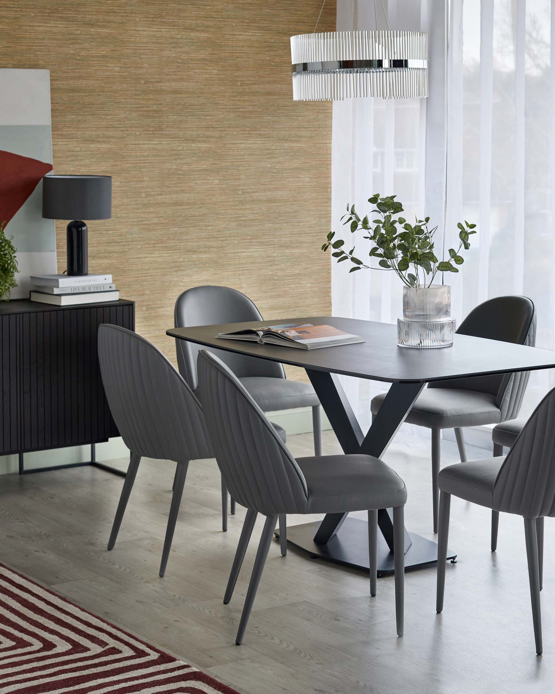 Modern dining setup featuring a sleek black table, gray ribbed chairs, a stylish lamp, and decorative plant accents.