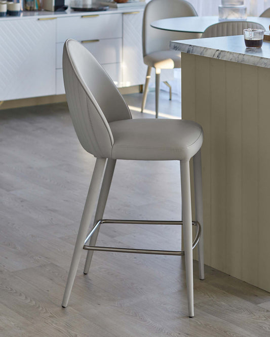 Stylish light grey upholstered barstool with a curved back and metal footrest, set in a modern kitchen environment.