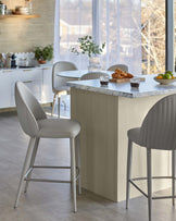 Stylish modern bar stools with soft cushioning and ribbed backs, paired with a sleek marble-topped kitchen island.