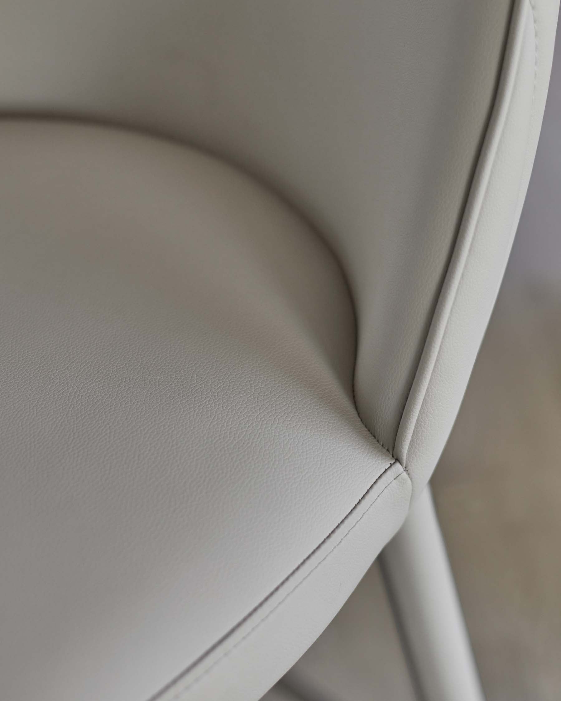 Close-up of a modern, light gray upholstered chair with smooth leather and sleek lines, emphasizing comfort and style.