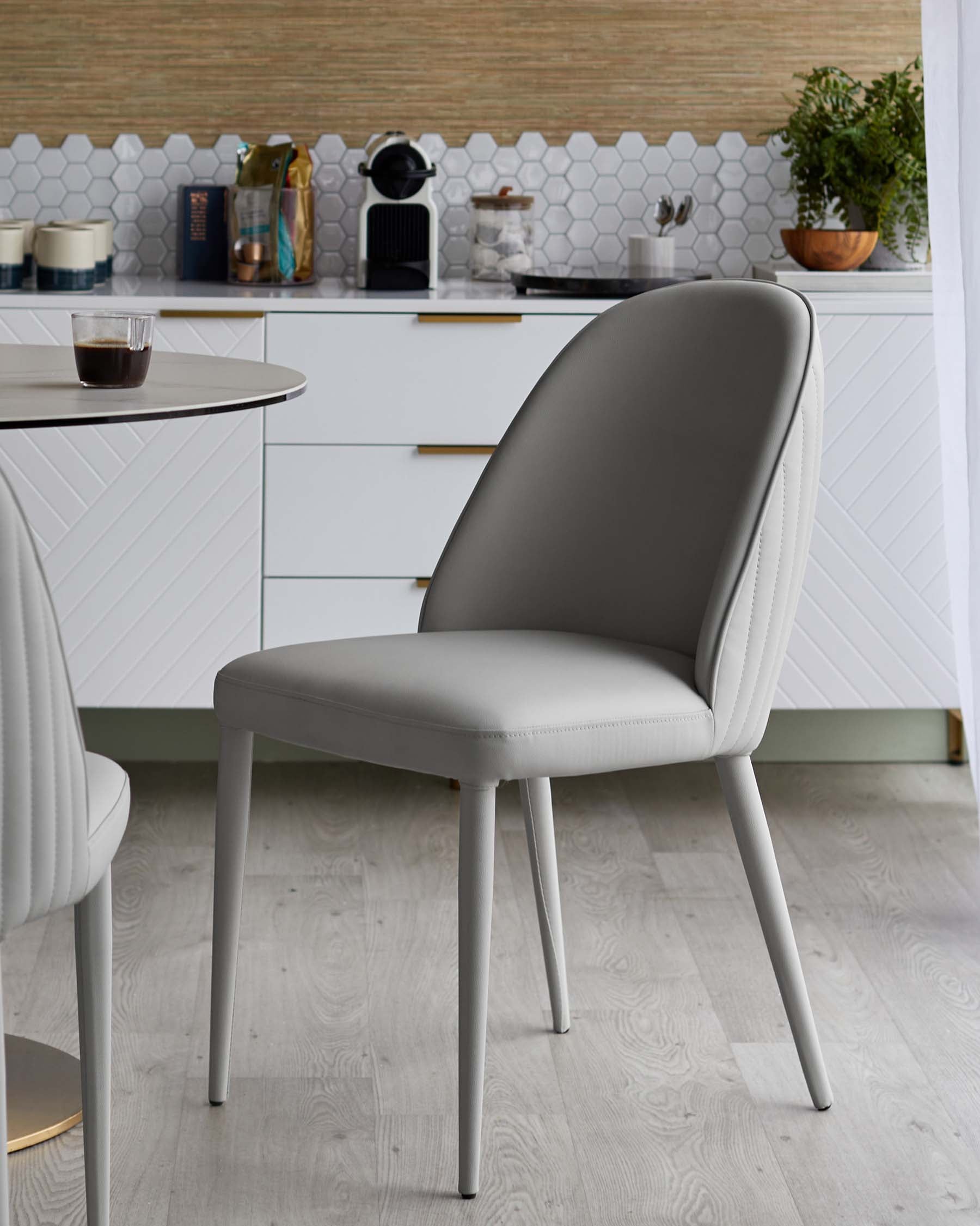 A sleek, modern gray dining chair with a curved back and slim legs, paired with a round tabletop in a stylish kitchen setting.